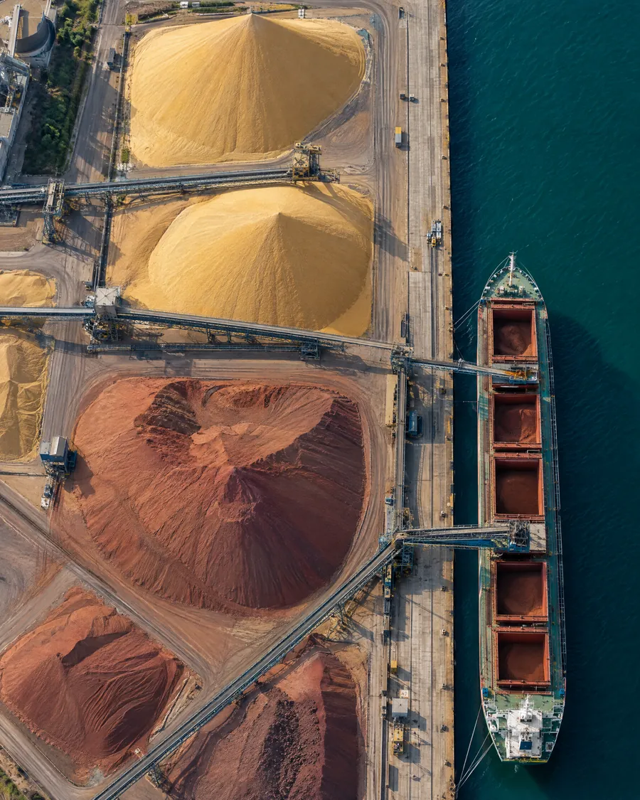 Aerial view of grain and ore piles at a harbour terminal beside a bulk carrier